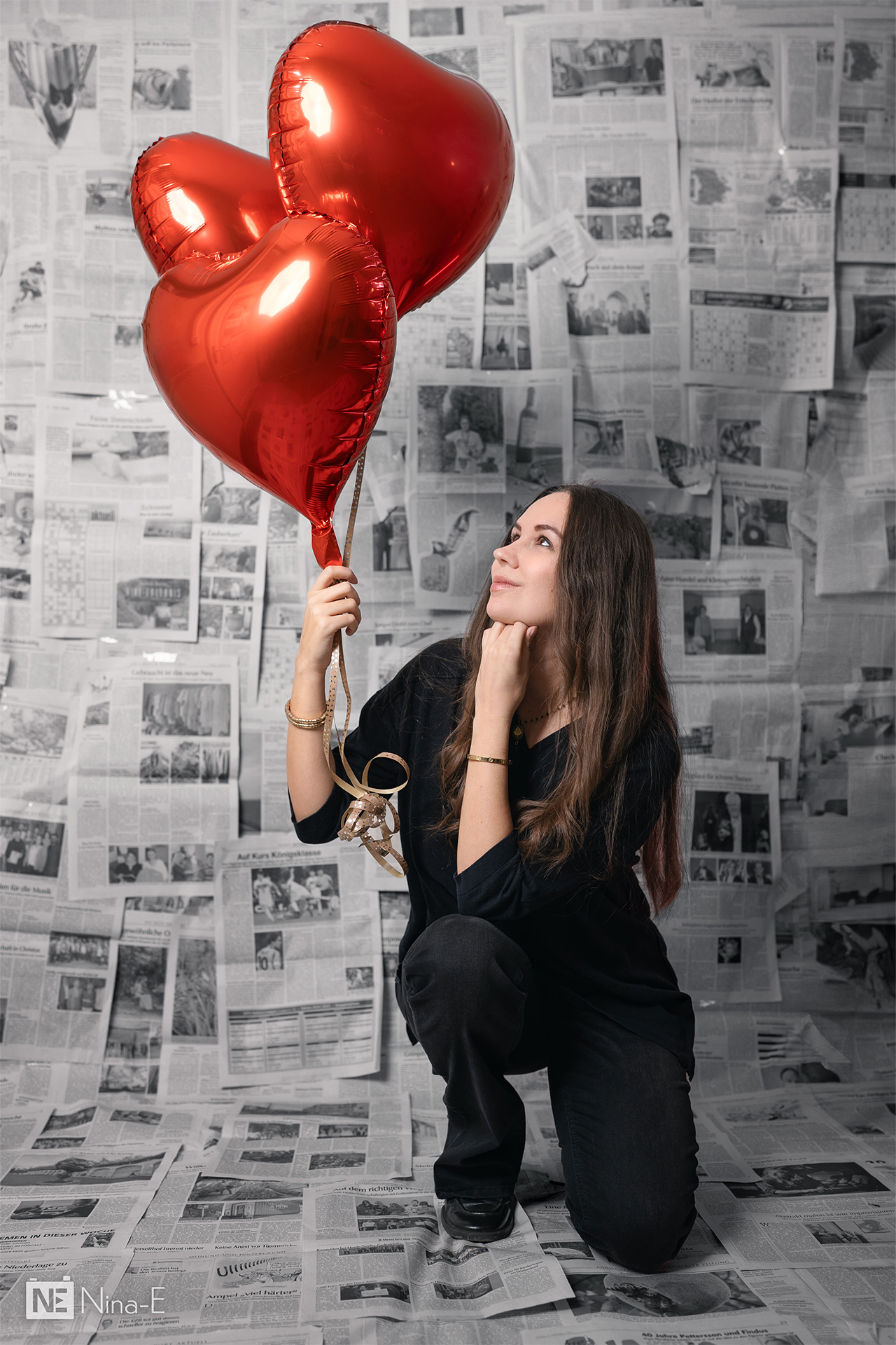 Frau mit roten Herzluftballons kniet vor Zeitungshintergrund