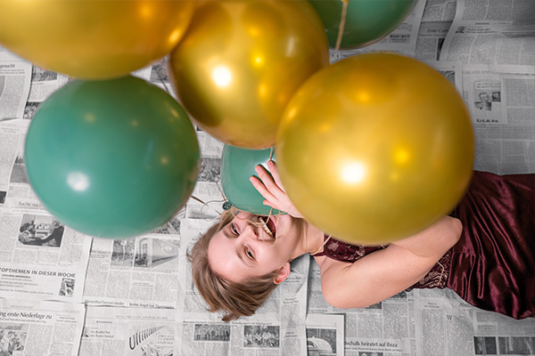 Person liegt auf Zeitungen und spielt mit Luftballons